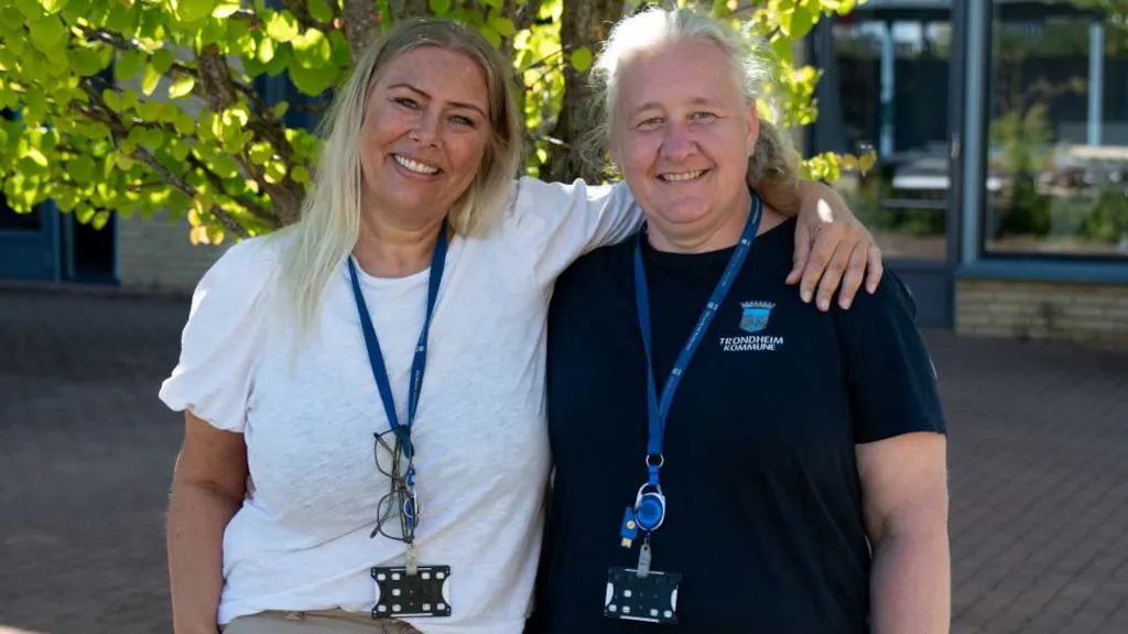 Bilde av driftskoordinator Rikke, og renholdsoperatør Aina. De står foran et tre, side om side og smiler. Rikke har armen sin rundt Aina sin skulder.