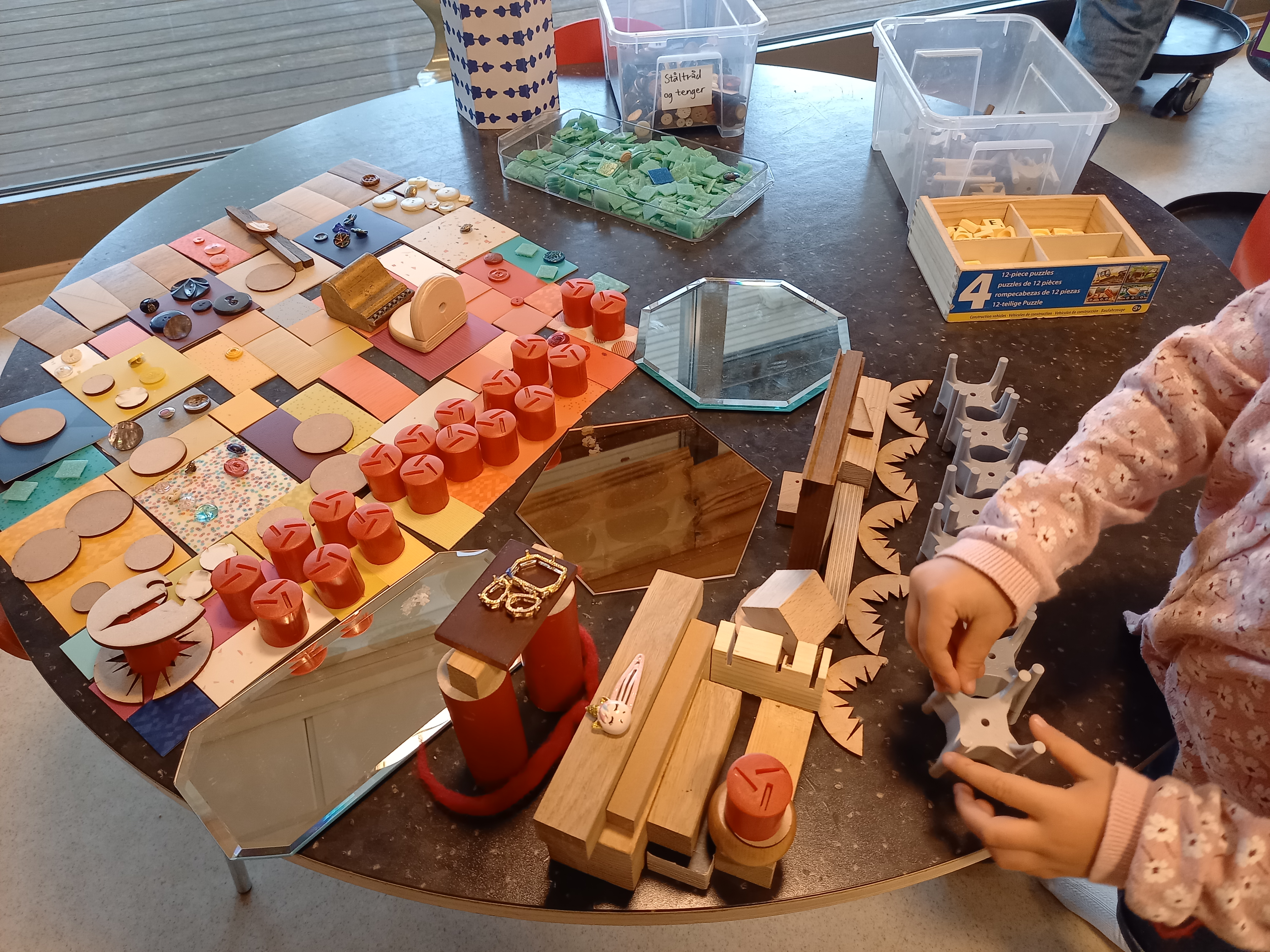 Bilde av et bord med mye ulikt åpent materiale, systematisk dandert av barn.