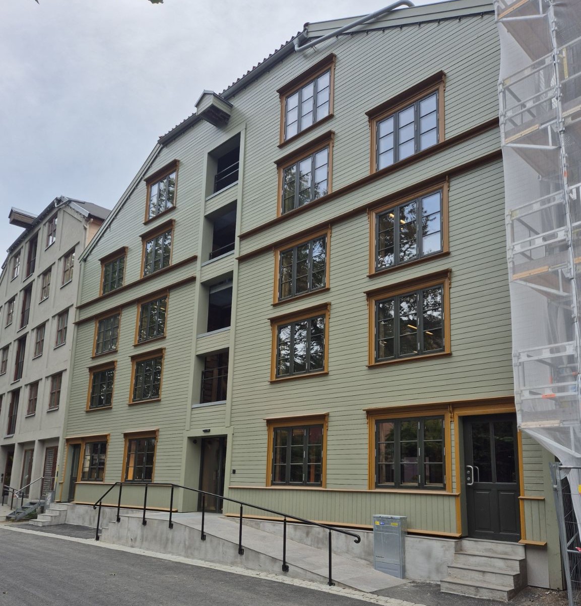 bygning i 4-5 etasjer med gr&oslash;nn panelkledning og brune vinduer