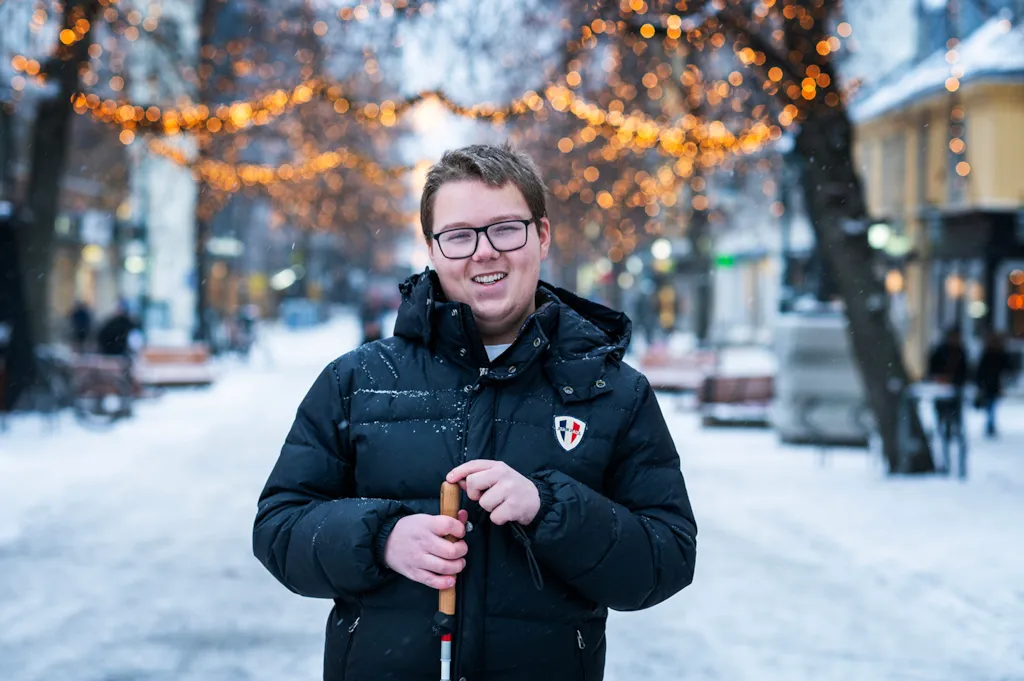 Smilende mann med blindestokk i snødekt gate