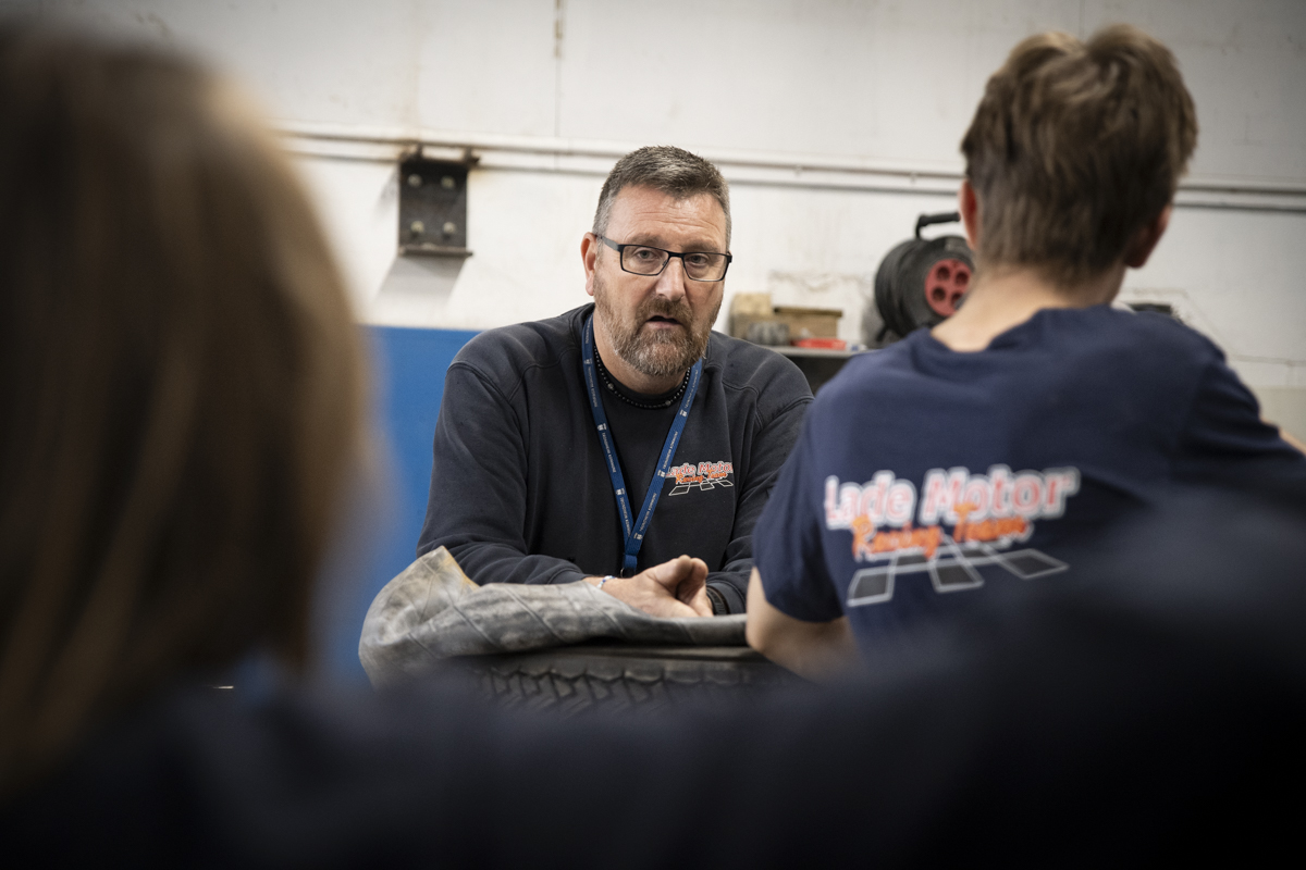 En godt voksen mann med skjegg snakker med ungdomsgutter i verkstedet.