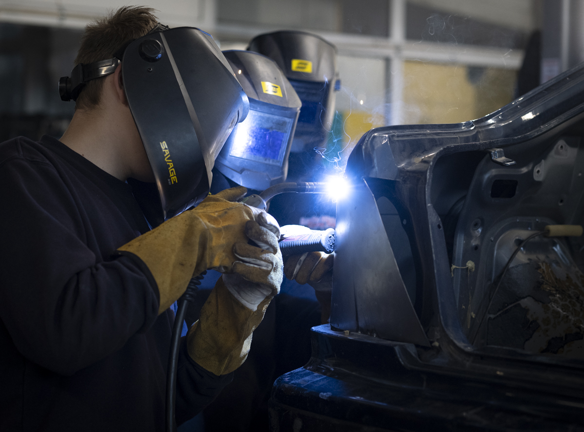 Bildet viser to personer med sveisemaske på, som sveiser på en bil.