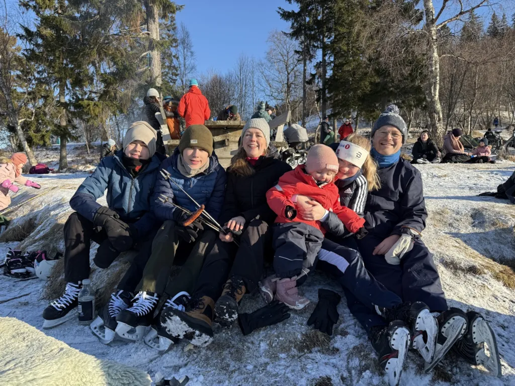 En familie med mor, far og fire barn sitter ved bålet. Alle har på seg skøyter.