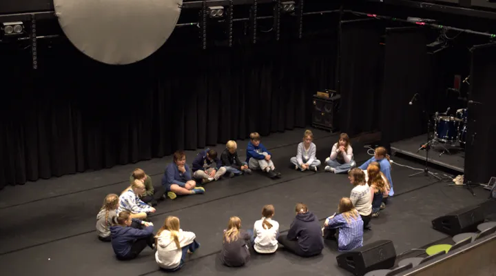 Elever undervises i joik og sitter i ring på scene.