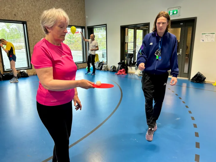 En av deltagerne balanserer en pingpongball mens instruktøren ser påInstruktør