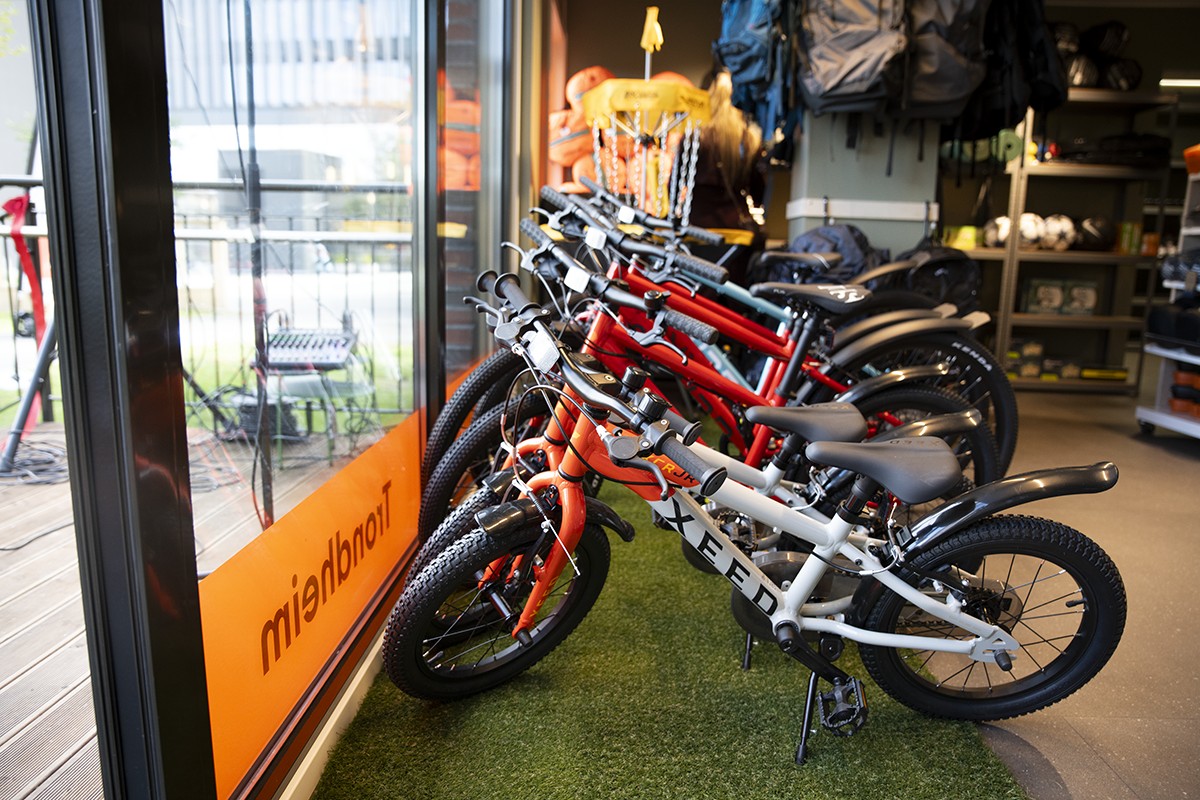 Bildet viser en rekke med barnesykler, og en hylle med friluftsliv i bakgrunnen.