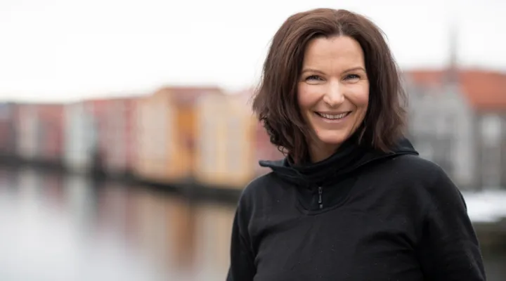 Portrett av parkeringsbetjent Marie på Gamle Bybro med Nidelva og bryggerekken i bakgrunnen.