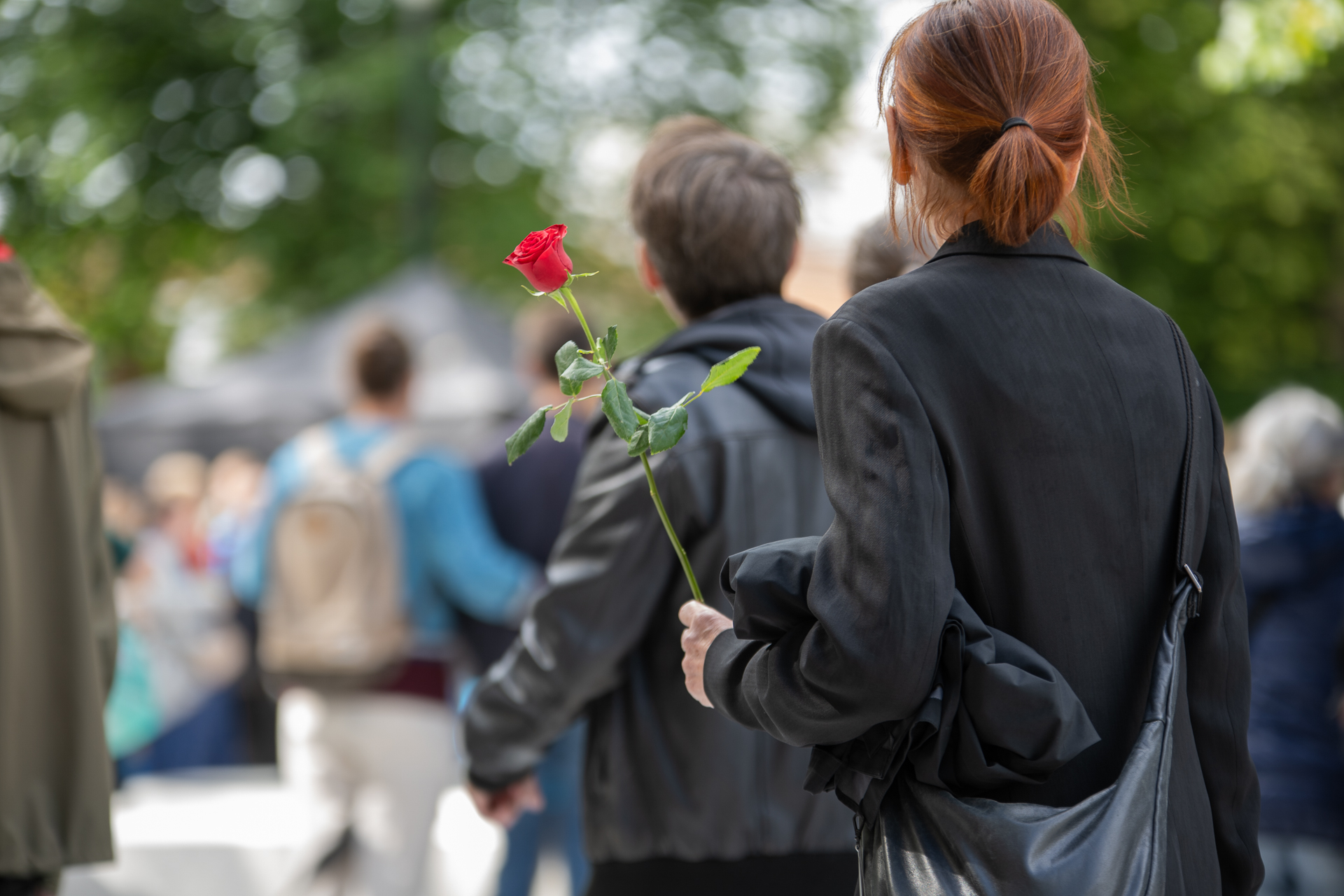 To personer står med ryggen til. En har rose i hånden