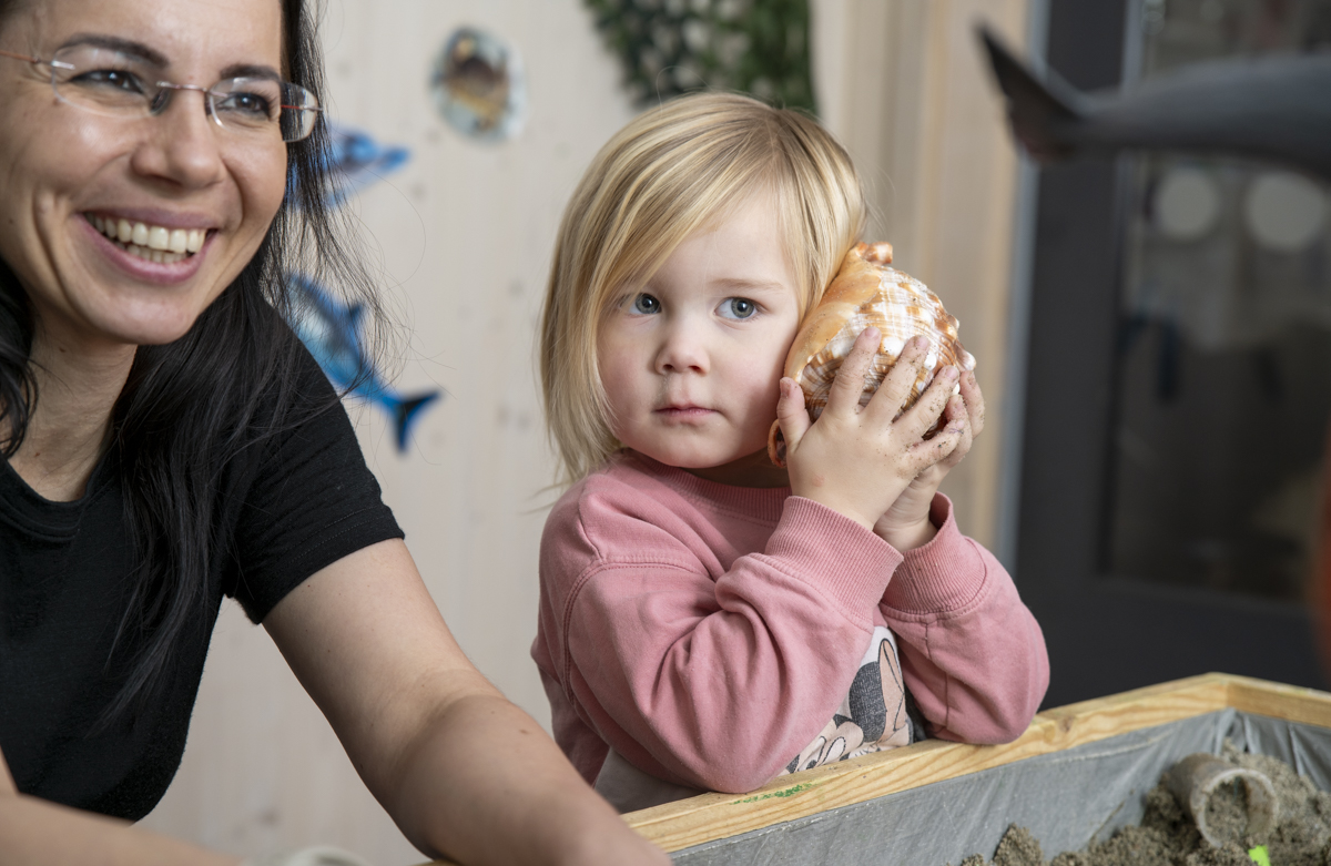 Ansatt sammen med barn som lytter i en stor konkylie