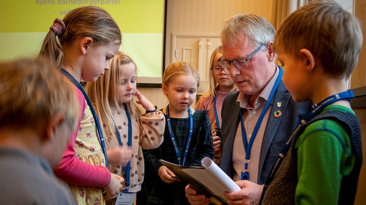 kommunedirekt&oslash;r Wolden leser i heftet han har f&aring;tt av de seks barna som st&aring;r rundt ham. Han st&aring;r p&aring; kne for &aring; v&aelig;re i samme h&oslash;yde.