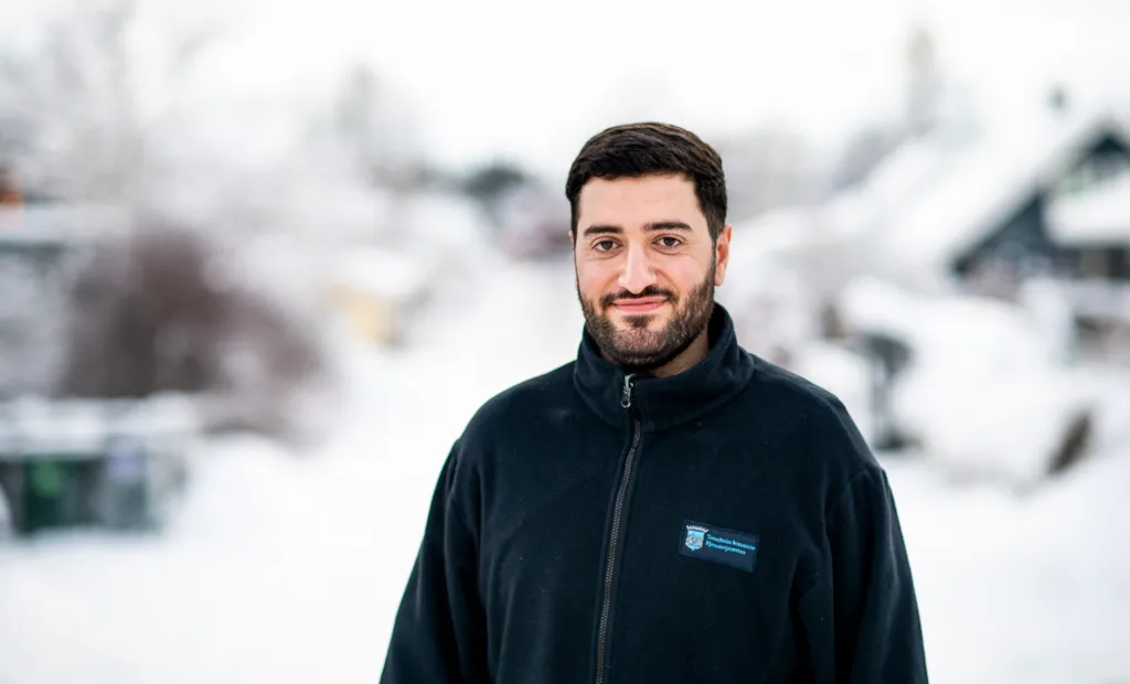 Malik står i en snødekt gate og smiler til kamera.