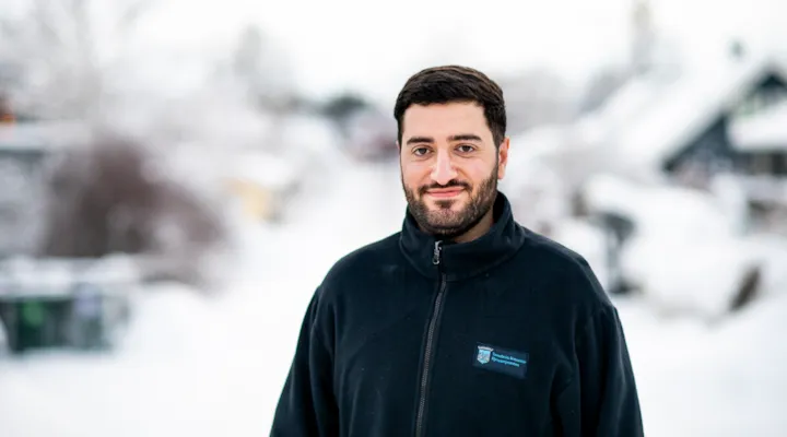 Malik står i en snødekt gate og smiler til kamera.