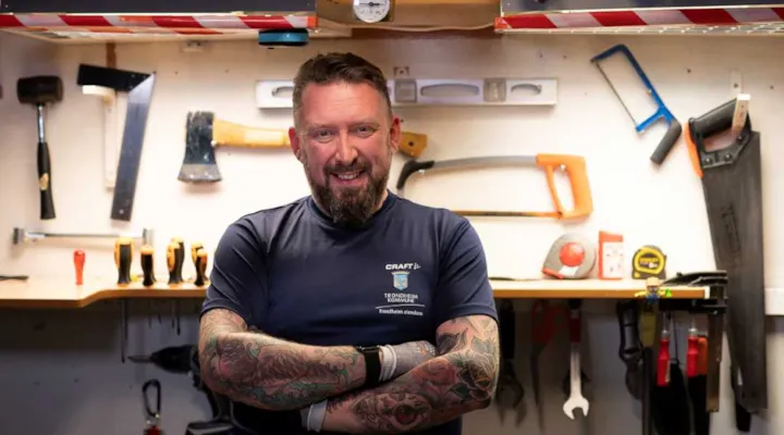Driftsoperatør Kim Roger Olsen står foran verktøybenken med ansiktet vendt mot kameraet. I bakgrunnen ser vi verktøy som henger på veggen.