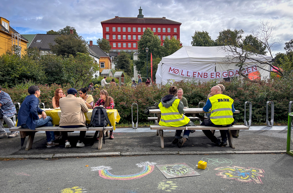 Folk sitter på benker med Bispehaugen skole i bakgrunnen