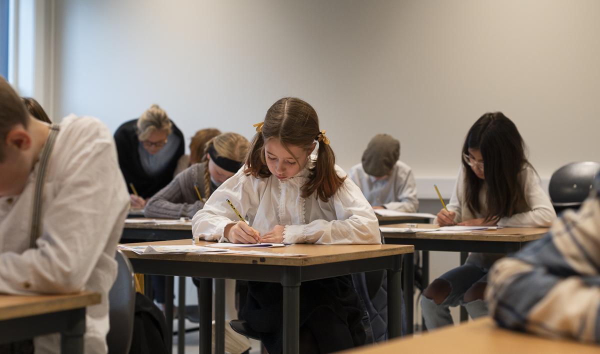 Seks elever sitter ved pultene sine og konsentrerer seg om &aring; skrive l&oslash;kkeskrift.