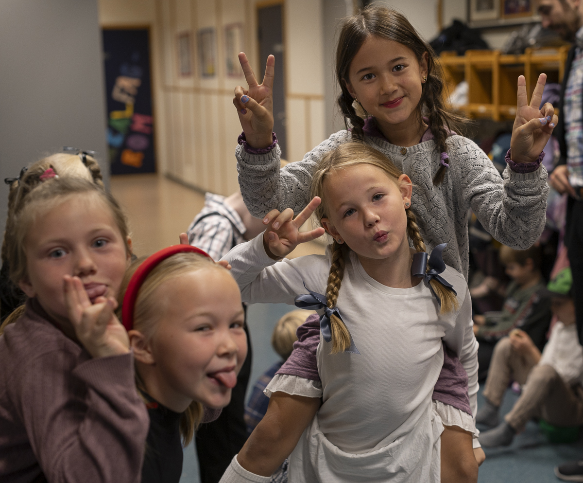 Fire jenter i 3. klasse tuller og smiler til kamera. De har flettet hår med sløyfer i og gammeldagse klær.