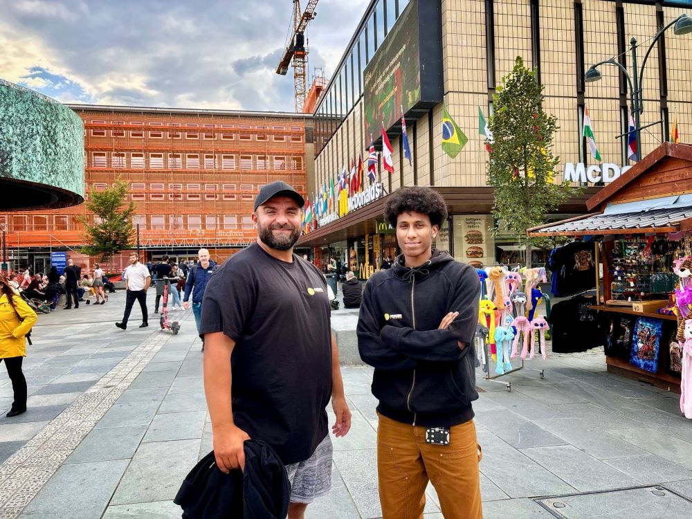 Riad og Efrem står på Trondheim torg og smilar mot kamera. Dei har på seg svart t-skjorte og genser med Uteseksjonen sin logo.