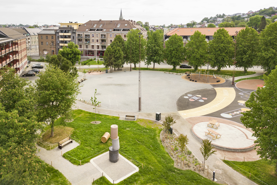 Oversiktsbilde med skateområde. Trær, hus og lekeapparat i bakgrunnen.