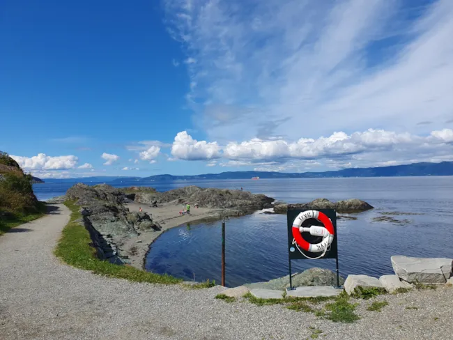 Foto av sandstrand ved fjorden med redningsbøye i forkant