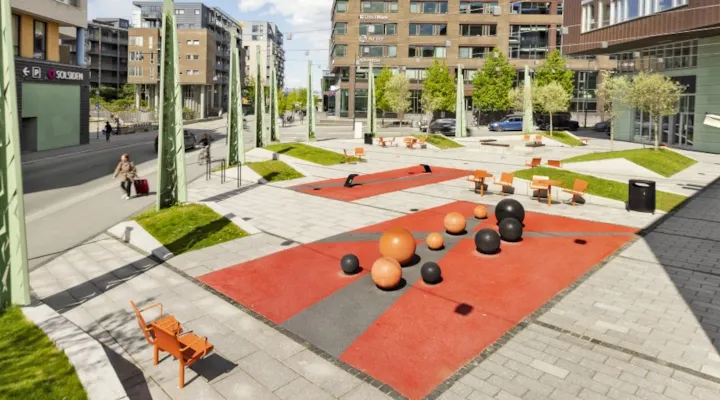 Benker og balanse-apparat på en plass med betongheller mellom høye bygg.