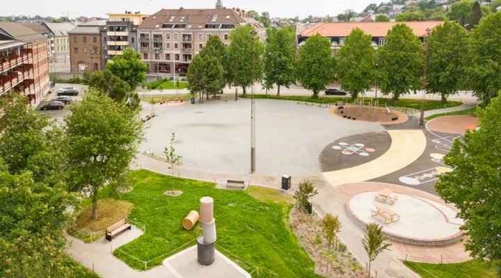 Oversiktsbilde med skateområde. Trær, hus og lekeapparat i bakgrunnen.