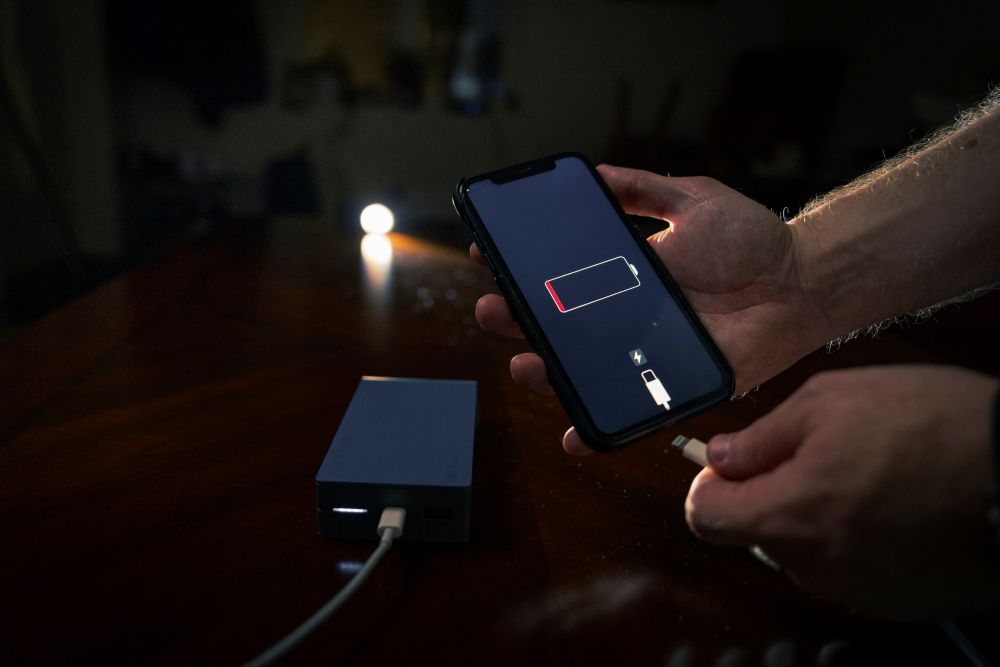 En person holder en smarttelefon med lavt batteri og er i ferd med &aring; koble til en ladekabel fra en n&oslash;dlader (powerbank).