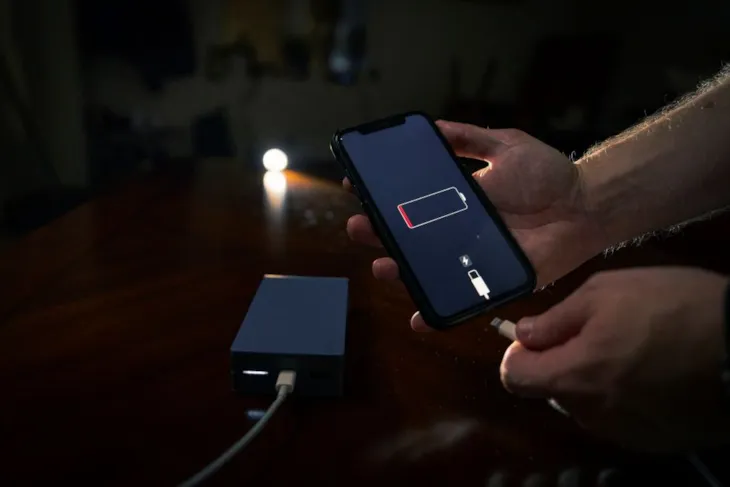 En person holder en smarttelefon med lavt batteri og er i ferd med å koble til en ladekabel fra en nødlader (powerbank).