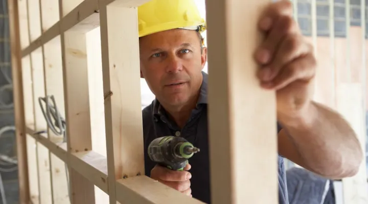 Mann med hjelm og drill som står mellom stendere