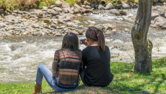To unge jenter som sitter ved ei lita elv. Bildet skal illustrere tankefull ungdom.
