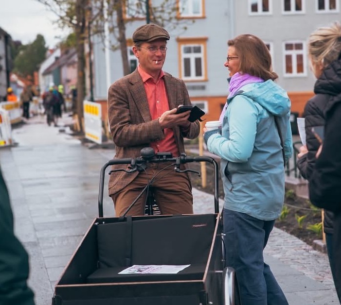 Trond &Aring;m sykler p&aring; lastesykkel og snakker med dame
