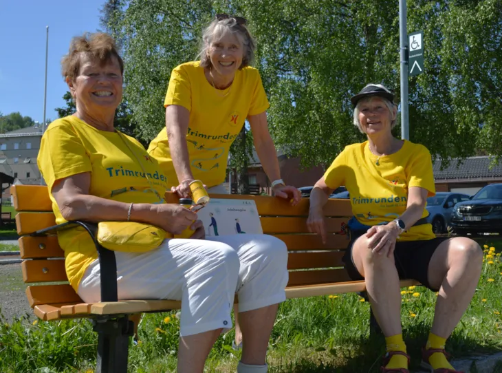 Tre ansatte med gule skjorter på en benk