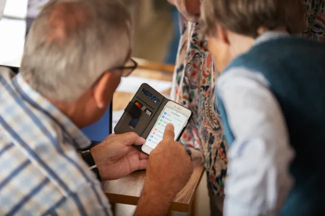 Eldre mann veileder eldre dame i bruk av smarttelefon