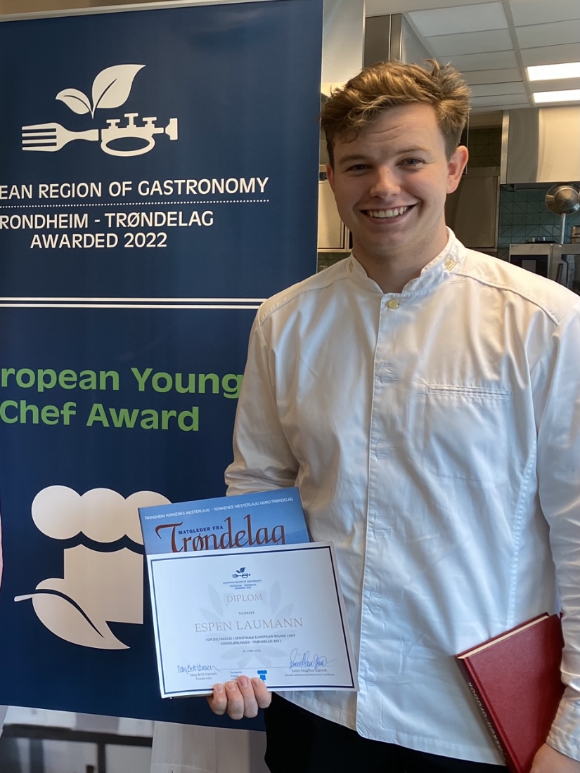 Bilde av Espen Laumann med diplom i hånda. Han står ved siden av en roll up hvor det står European Region of Gastronomy 2022, Young chef award.